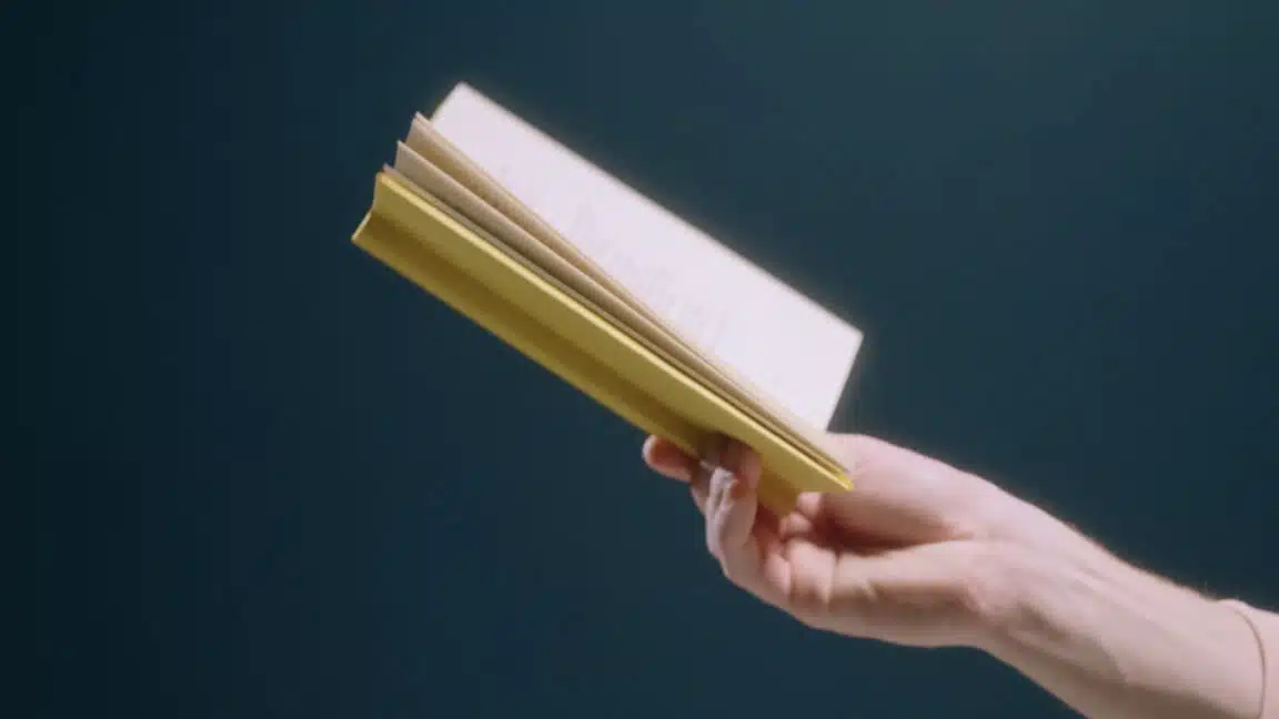 Hand holding book in front of green background - blog on sales management